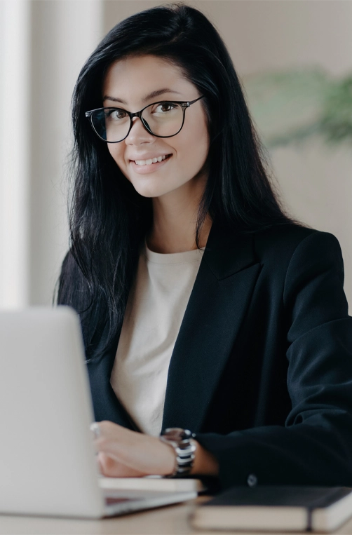 Smiling well-dressed woman secretary works on laptop at a modern office desk, conducting project or research work